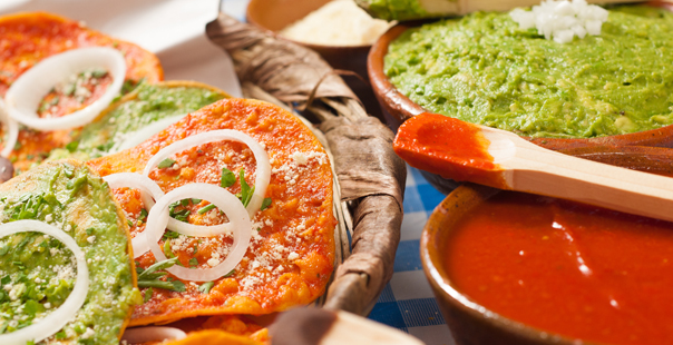 Tostadas of guacamole, tomato sauce and black beans, and bowls with different sauces, and wooden spoons.